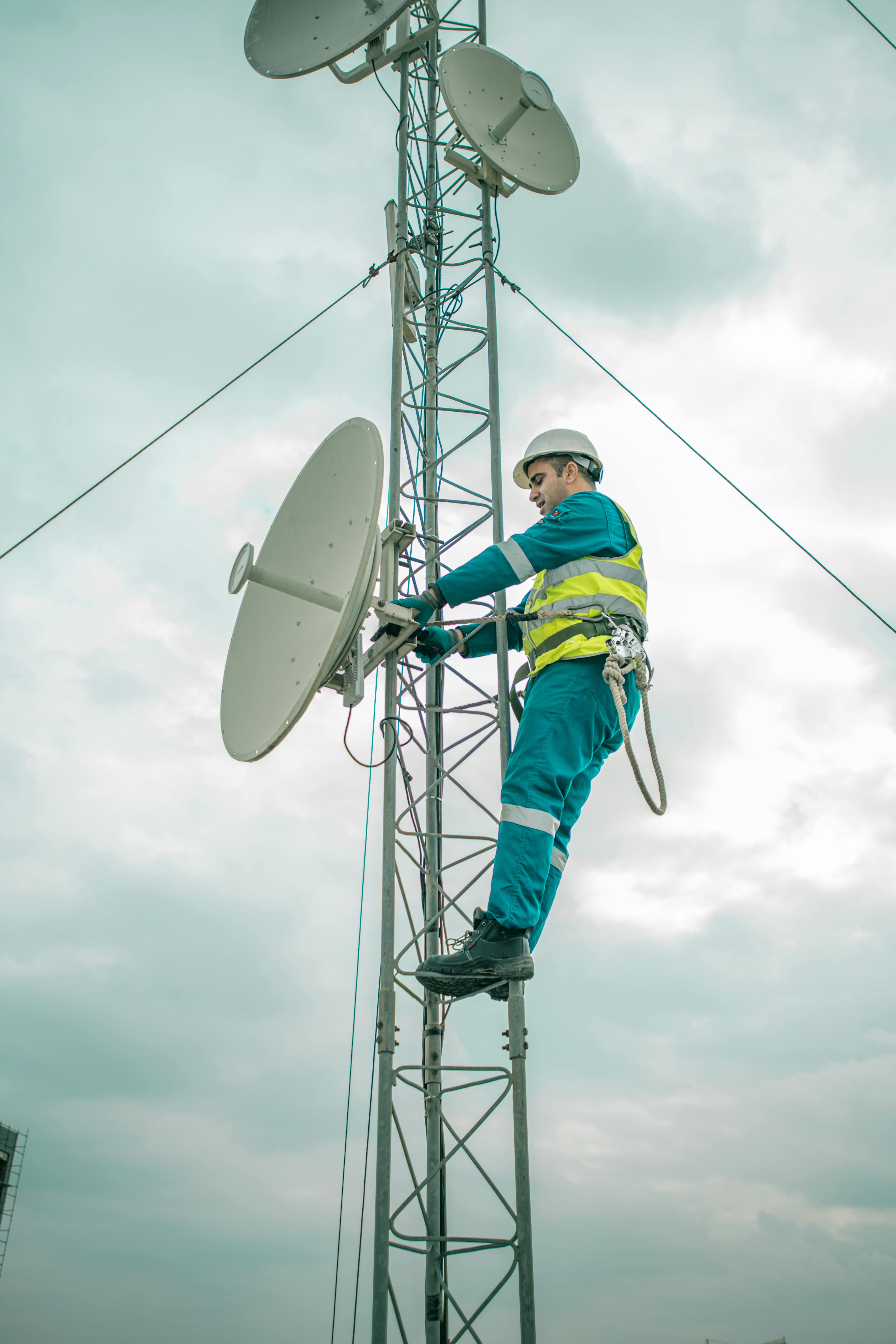 Técnico em telecomunicações trabalhando no topo de uma torre de celular.